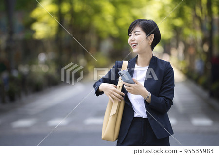 一位女商人走在辦公區，一隻手拿著智能手機 95535983