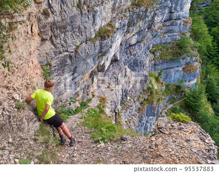 Boy at top of path with steel chain anchored in the rocky wall Boy at top of path with steel chain anchored in the rocky wall 95537883