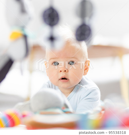 Cute baby boy playing with hanging toys arch on mat at home Baby activity and play center for early infant development. Baby playing at home 95538318