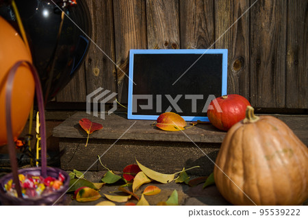 Selective focus. A blackboard with copy advertising space, next to pumpkins on a wooden threshold with fallen yellow and red leaves in autumn. Porch or backyard decoration. Halloween trick and treat Selective focus. A blackboard with copy advertising space, next to pumpkins on a wooden threshold with fallen yellow and red leaves in autumn. Porch or backyard decoration. Halloween trick and treat 95539222