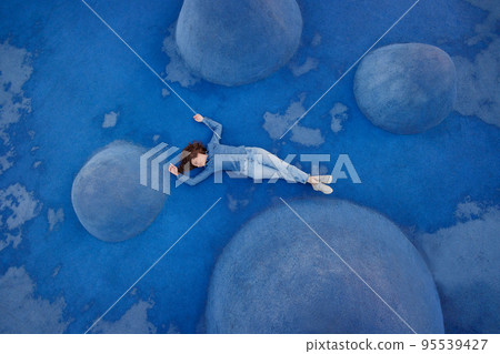 woman in blue jeans and a shirt is lying on a blue background on a sports field or in a park. a combination of colors, 95539427