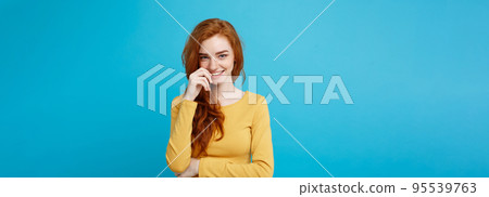 Lifestyle concept - Close up Portrait young beautiful attractive ginger red hair girl playing with her hair with shyness. Blue Pastel Background. Copy space. 95539763