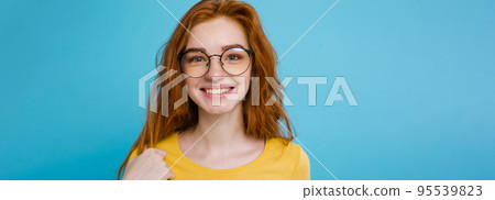Headshot Portrait of happy ginger red hair girl with freckles smiling looking at camera. Pastel blue background. Copy Space 95539823