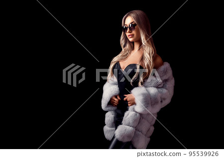 Glamour blonde girl posing in luxurious fur coat and sunglasses while standing on black background 95539926