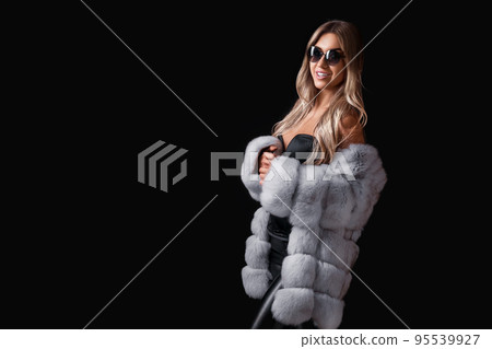 Attractive blonde girl in sunglasses posing on a black background in a fur coat. Commercial concept Attractive blonde girl in sunglasses posing on a black background in a fur coat. Commercial concept 95539927