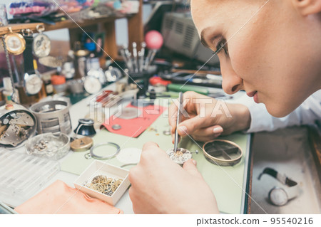 Woman watchmaker working diligently on repairing a watch Woman watchmaker working diligently on repairing a watch 95540216