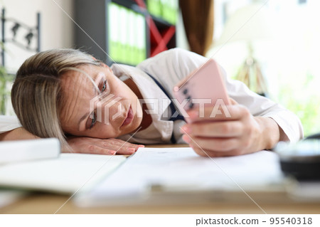 Tired doctor putting head on table and surfing internet on smartphone Tired doctor putting head on table and surfing internet on smartphone 95540318