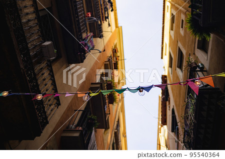 Colorful triangular flag garlands hanging over a busy street on Valencia, Spain. Green, yellow and red buntings as an outdoor decoration. Colorful triangular flag garlands hanging over a busy street on Valencia, Spain. Green, yellow and red buntings as an outdoor decoration. 95540364