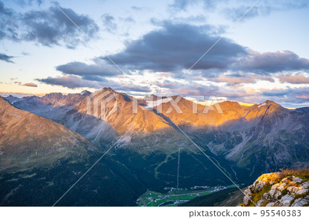 Alpine mountain peaks illuminated by rising sun Alpine mountain peaks illuminated by rising sun 95540383