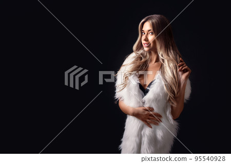 Beautiful blonde girl posing in luxurious white fur cape while standing on black background. Fashion Beautiful blonde girl posing in luxurious white fur cape while standing on black background. Fashion 95540928