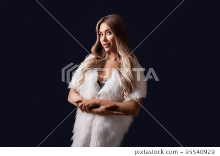 Attractive blonde girl posing in luxurious fur cape while standing on black background. Fashion 95540929