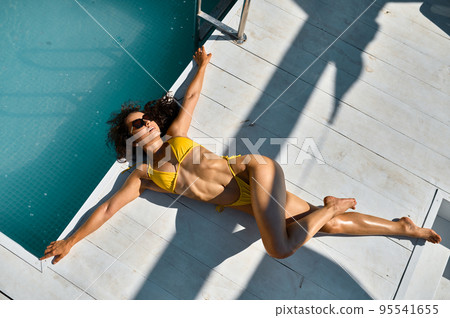 Attractive young woman relaxing lying at poolside Attractive young woman relaxing lying at poolside 95541655