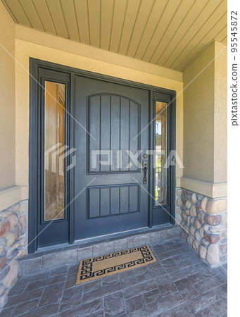 Vertical Porch of a house with stone tiles flooring and black front door with two side panels 95545872
