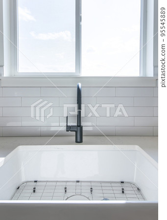 Vertical White porcelain sink with black single faucet in a kitchen against the window Vertical White porcelain sink with black single faucet in a kitchen against the window 95545889