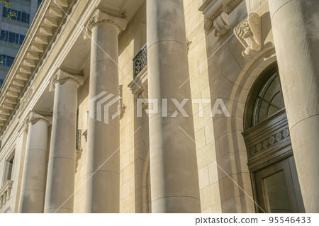 Exterior of a building with huge circular columns and brown wooden door 95546433