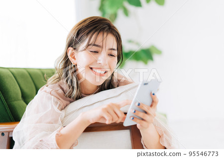 一個女人躺在沙發上,看著她的智能手機 一個女人躺在沙發上,看著她的智能手機 95546773