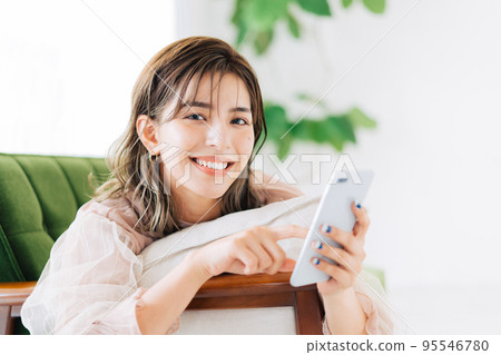 A woman lying on the sofa and holding a smartphone 95546780