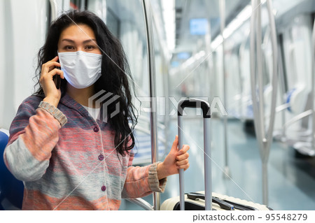 Woman traveler in a protective mask talking on a mobile phone in subway car Woman traveler in a protective mask talking on a mobile phone in subway car 95548279