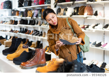 Woman choosing boots in shoeshop Woman choosing boots in shoeshop 95548326