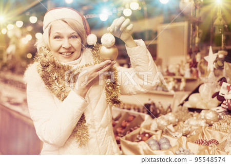Smiling woman is buying toys for X-mas tree in the market Smiling woman is buying toys for X-mas tree in the market 95548574