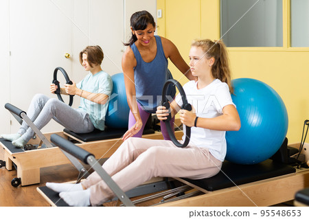 Pilates instructor helps teenager do exercises with ring 95548653