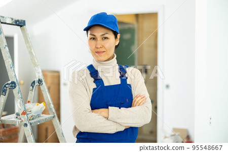 Portrait of positive builder woman in blue overalls next to stepladder Portrait of positive builder woman in blue overalls next to stepladder 95548667