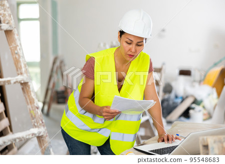 Woman builder checking project documentation and using laptop Woman builder checking project documentation and using laptop 95548683