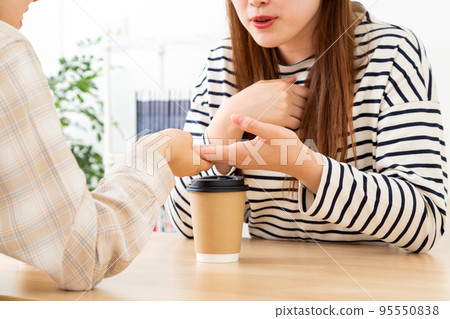 Two young women talking in a cafe while looking at hands 95550838