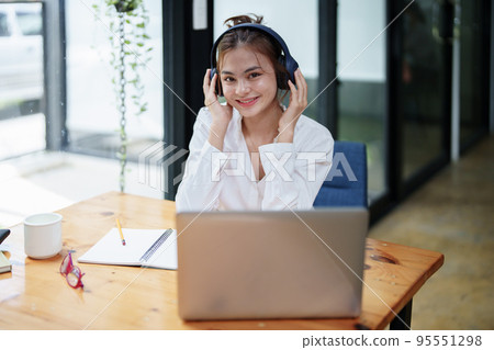 Portrait of a beautiful woman using a computer and earphone during a video conference Portrait of a beautiful woman using a computer and earphone during a video conference 95551298