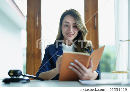 Portrait of a young Asian lawyer studying a lawsuit for a client using notebooks and paperwork on a desk. 95551439