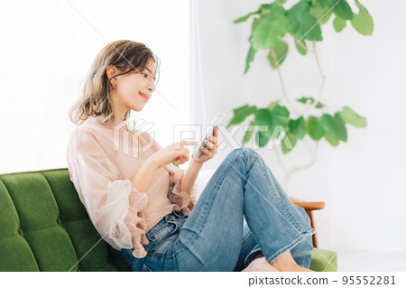 A young woman sitting on the sofa and operating a smartphone A young woman sitting on the sofa and operating a smartphone 95552281