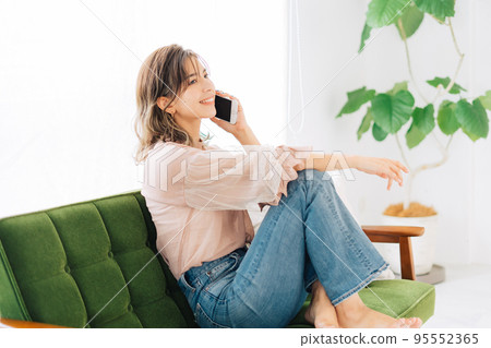 Young woman sitting on the sofa and making a phone call 95552365