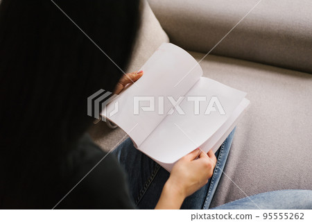 Woman is reading a book, a mockup of a blank page. View from behind the girl's shoulder on the book 95555262