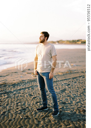 Young man stands on a sandy beach and looks at the sea 95556512