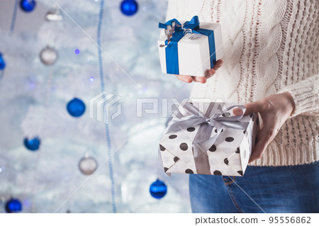 woman in white sweater and jeans in front of Christmas tree with present woman in white sweater and jeans in front of Christmas tree with present 95556862