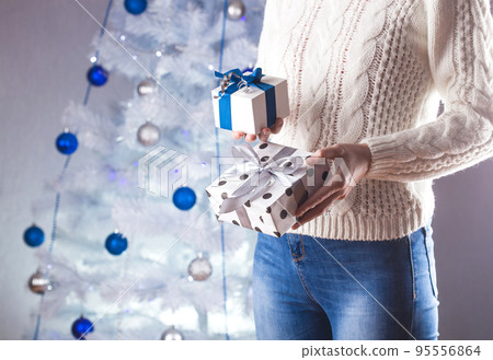 woman in white sweater and jeans in front of Christmas tree with present woman in white sweater and jeans in front of Christmas tree with present 95556864