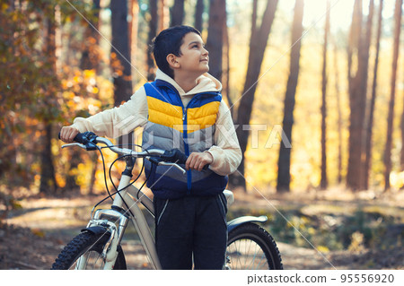 Happy kid boy having fun in autumn forest with a bicycle on beautiful fall day. Happy kid boy having fun in autumn forest with a bicycle on beautiful fall day. 95556920