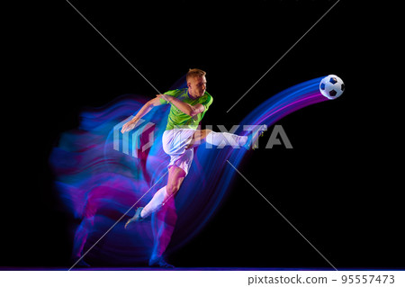 Goal. Young soccer, football player in motion and action with ball isolated on dark background in neon mixed light. Concept of achievement, creativity, sport, energy, championship Goal. Young soccer, football player in motion and action with ball isolated on dark background in neon mixed light. Concept of achievement, creativity, sport, energy, championship 95557473