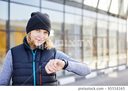 Fit woman looking at smartwatch and counting calories burned. Woman standing relaxed after workout checking heart rate with smartwatch. Happy runner checking smartwatch after exercising outdoors 95558165