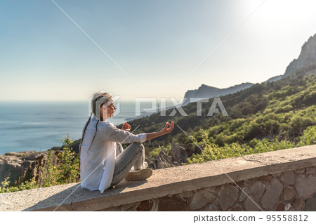 Profile of a woman doing yoga in the top of a cliff in the mountain. Woman meditates in yoga asana Padmasana Profile of a woman doing yoga in the top of a cliff in the mountain. Woman meditates in yoga asana Padmasana 95558812