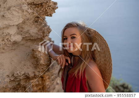 A woman in a red flying dress fluttering in the wind, against the backdrop of the sea. A woman in a red flying dress fluttering in the wind, against the backdrop of the sea. 95558857