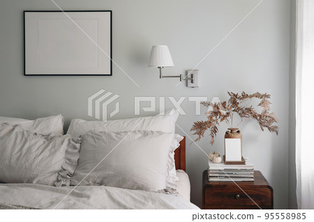 Greeting card mockup on wooden bedsife table with books, white pumpkins and dry fern in vase. Blank black picture frame on sage green wall. Elegant bedroom view. Grey frilled linen pillows. Interior. Greeting card mockup on wooden bedsife table with books, white pumpkins and dry fern in vase. Blank black picture frame on sage green wall. Elegant bedroom view. Grey frilled linen pillows. Interior. 95558985