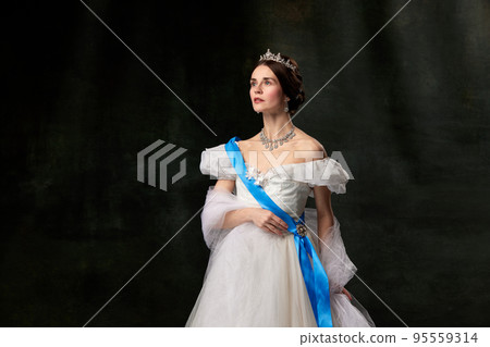Young queen. Portrait of adorable girl in image of medieval royal person in renaissance style dress isolated on dark background. Comparison of eras, beauty, history, art 95559314