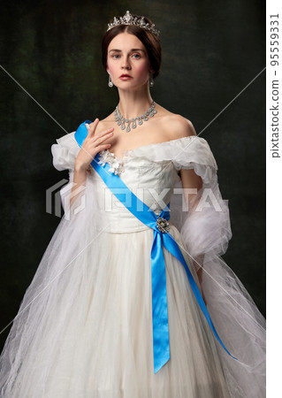Young queen. Portrait of adorable girl in image of medieval royal person in renaissance style dress isolated on dark background. Comparison of eras, beauty, history, art 95559331