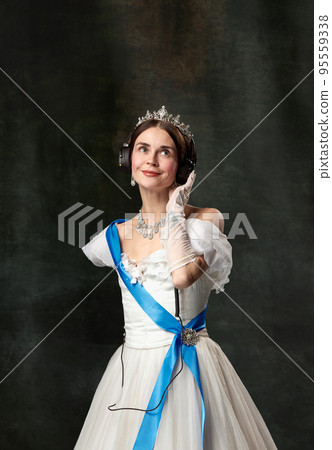 The favorite music. Elegant woman, royal person, queen or princess in white medieval outfit listening to music on dark vintage background. The favorite music. Elegant woman, royal person, queen or princess in white medieval outfit listening to music on dark vintage background. 95559338