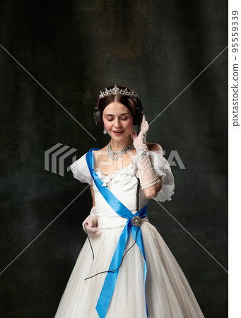 The favorite music. Elegant woman, royal person, queen or princess in white medieval outfit listening to music on dark vintage background. The favorite music. Elegant woman, royal person, queen or princess in white medieval outfit listening to music on dark vintage background. 95559339