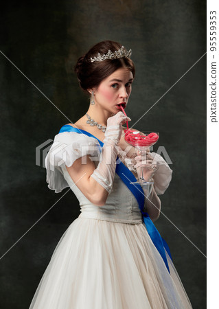 Sweet delight. Elegant woman, royal person, queen or princess in white medieval outfit tasting jelly candy on dark vintage background. 95559353