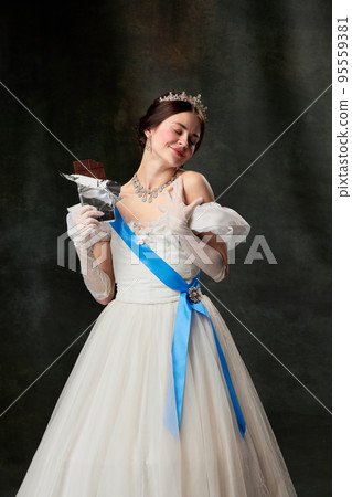 Sweet delight. Elegant woman, royal person, queen or princess in white medieval outfit tasting chocolate on dark vintage background. Sweet delight. Elegant woman, royal person, queen or princess in white medieval outfit tasting chocolate on dark vintage background. 95559381