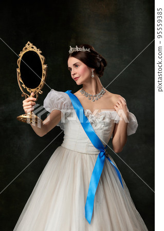Young queen. Portrait of adorable girl in image of medieval royal person in renaissance style dress isolated on dark background. Comparison of eras, beauty, history, art 95559385