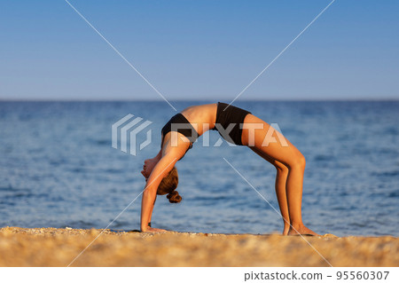 Young woman doing yoga wheel pose or Dhanurasana at the beach 95560307